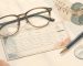 Illustration of eyeglasses, a pen, and an anonymized prescription card on a warm tabletop.